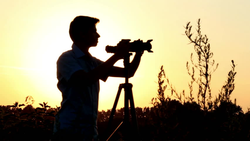 Young male shooting photo video at dusk, tripod camera shot