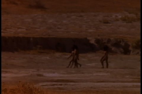 Historical reenactment in East Africa. Group of early humans, or Homo erectus, walk across dusty plain.