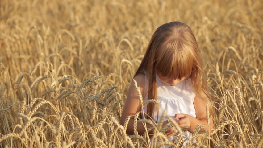 Cute little girl standing in wheat giving thumb up and smiling happily at camera