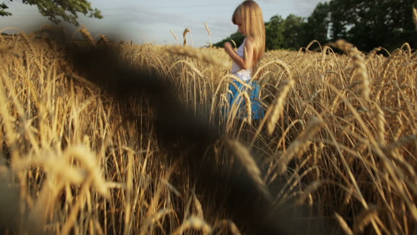 Pretty little girl standing in the middle of wheat field and smiling at camera