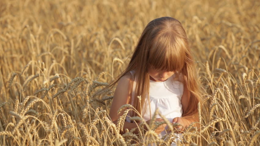 Pretty little girl standing in wheat field eating grain giving thumb up and