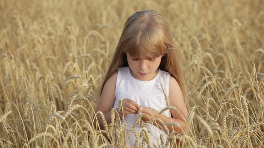 Cute little girl standing in wheat eating grain moving her hands and laughing