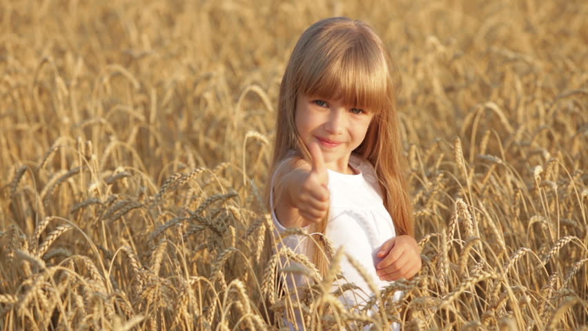 Pretty little girl standing in golden wheat giving thumb up and smiling at