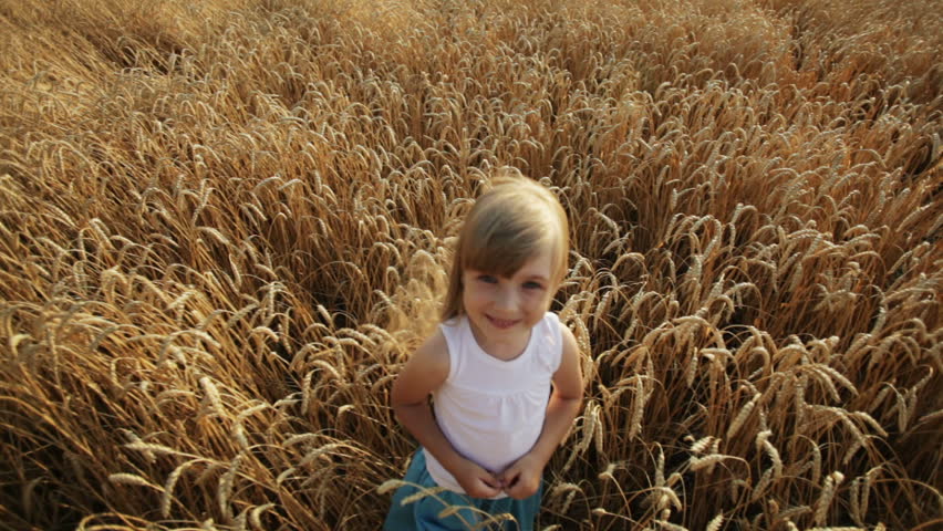 Beautiful little girl standing in wheat field smiling and waving her hand at