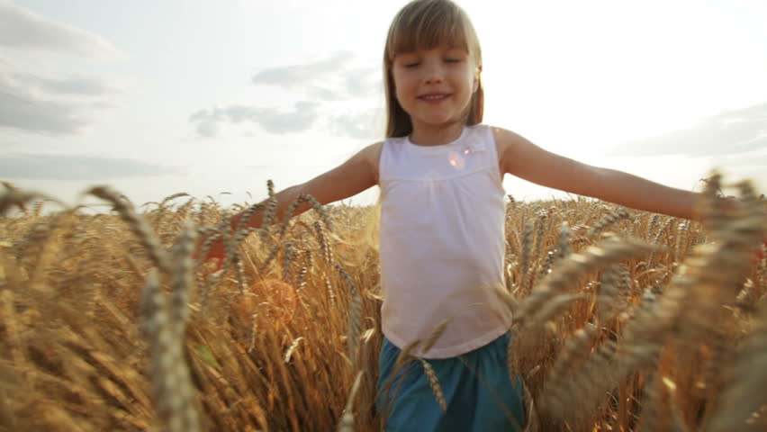 Pretty little girl walking through wheat field stretching out her arms and