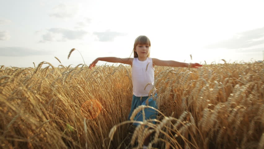 Joyful little girl walking on wheat field stretching out her arms and smiling