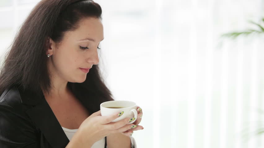 Pretty young woman drinking coffee looking at camera and smiling