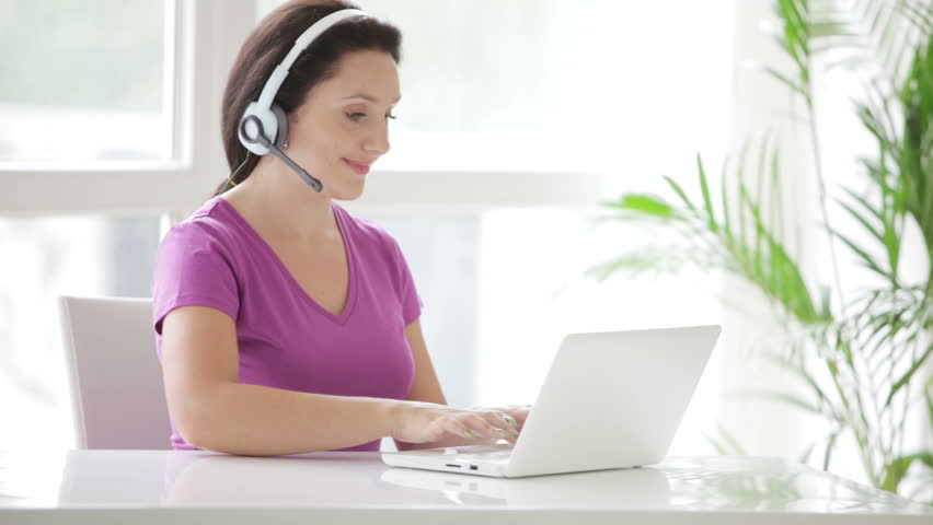 Pretty call centre operator in headset at work using laptop