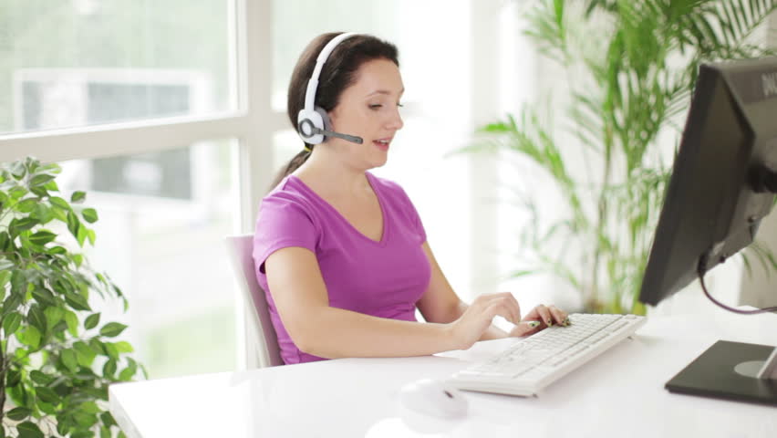 Cheerful call centre operator in headset at work using laptop