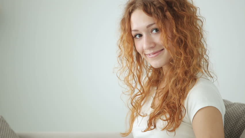 Pretty girl sitting on sofa using laptop and smiling at camera