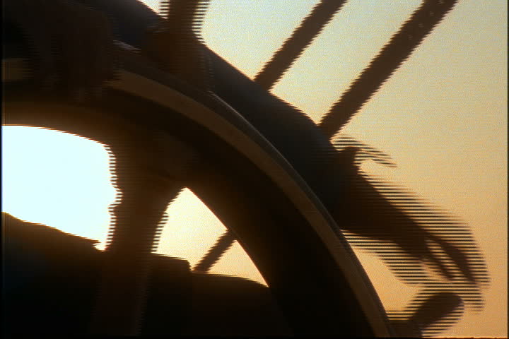 CU hands on wheel steering sailing ship at sunset in Bridgeport, Barbados.