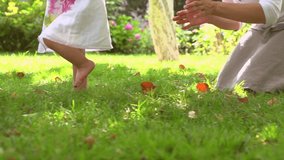 Adorable one year old Baby Girl making her first steps outdoor. Slow Motion Video Footage of the First Steps of the Kid. Sunny day and Green Grass 