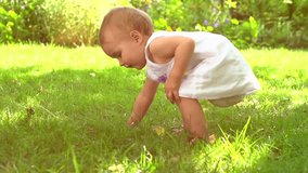 Adorable one year old Baby Girl making her first steps outdoor. Slow Motion Video Footage of the First Steps of the Kid. Sunny day and Green Grass. High speed camera 240 fps 