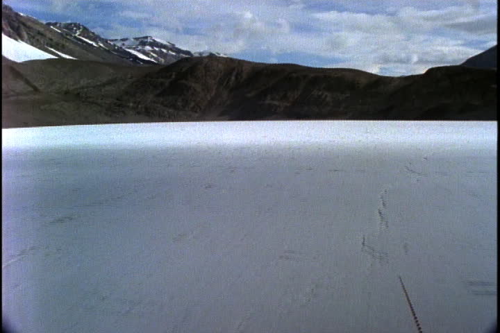 Camera moves fast over flat ice sheet towards dry land and mountains in Antarctica.