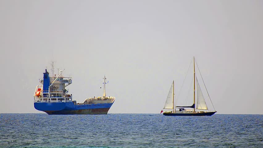 Sailboat in regatta on blue sea. Sailboat is passing near transportation tanker