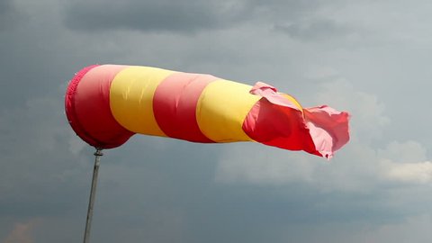 Wind sock with rainy stormy clouds background. Red and yellow