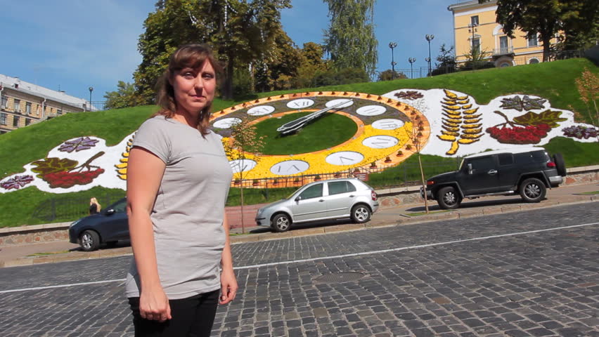 pretty woman looks at hour on real flower clock in center of Kiev