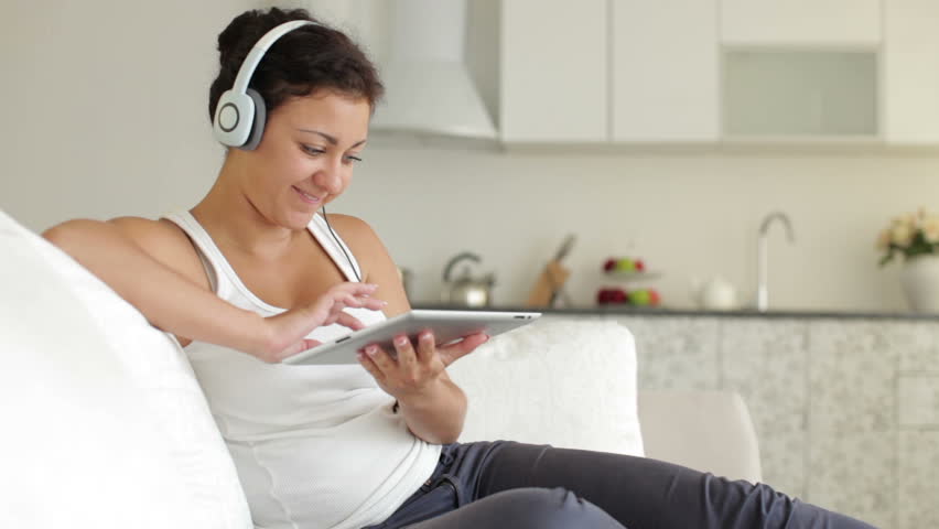 Young woman wearing headset relaxing on sofa with touchpad