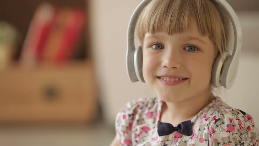 Cheerful little girl in headset smiling and laughing at camera