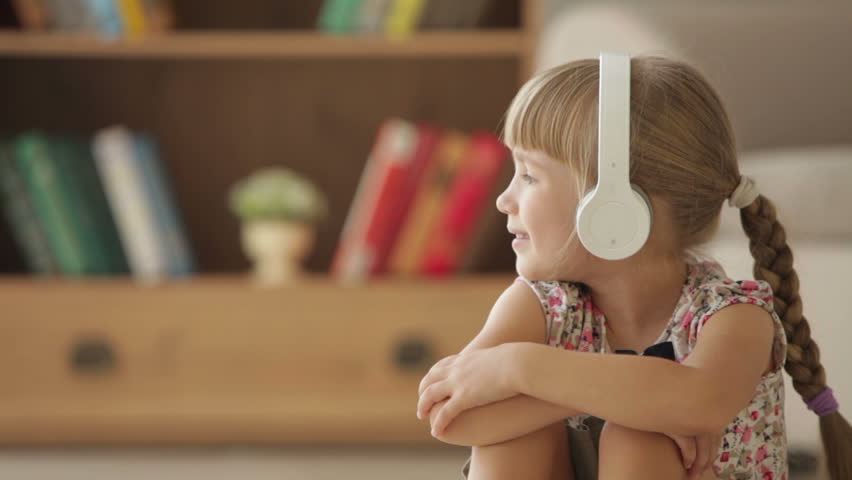 Cute little girl in headset listening to music singing and smiling at camera