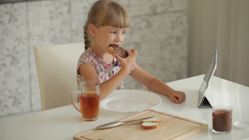 Beautiful little girl sitting at kitchen table eating chocolate sandwich