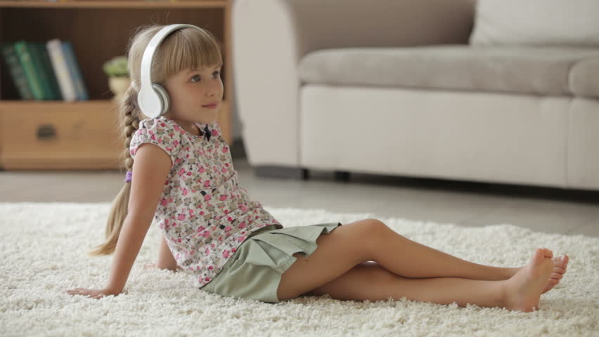 Beautiful little girl sitting on floor in living room listening to music on