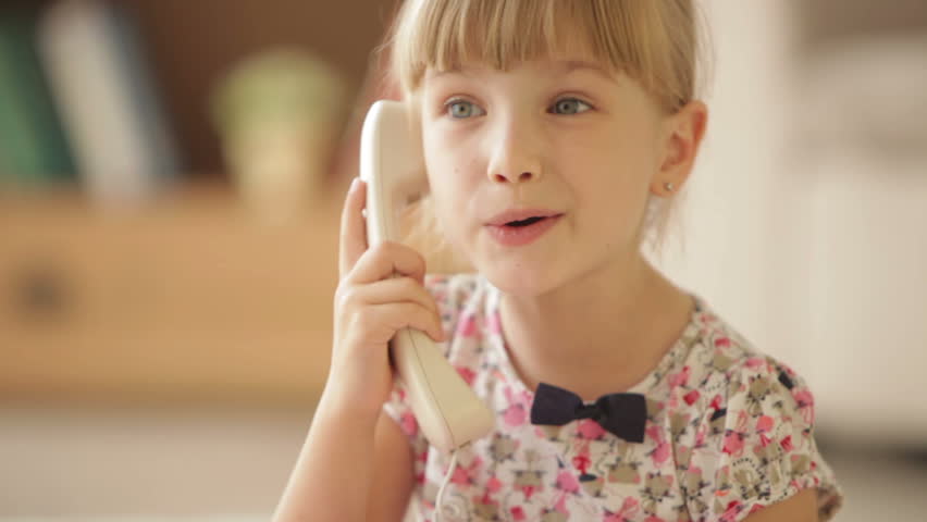 Cute little girl holding receiver talking on phone and laughing at camera
