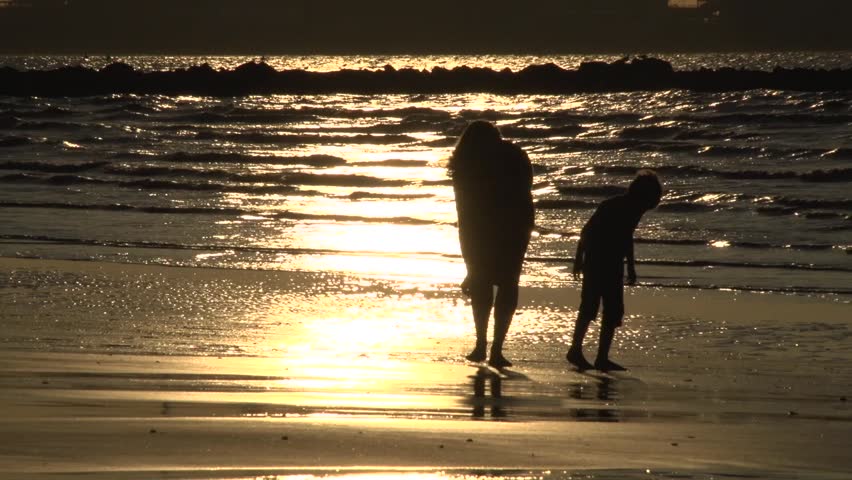 Mum and son silhouetted searching seashells at the beach