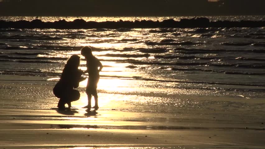 Mum and son silhouetted searching seashells at the beach