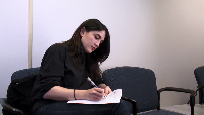 Young woman sitting on a chair, filling in paperwork.