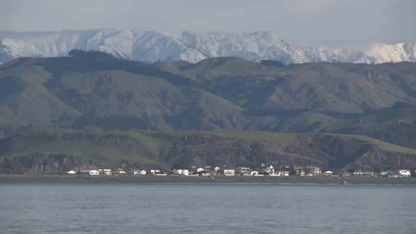 A fishing boat heads out to sea past a background of snow covered mountains.
