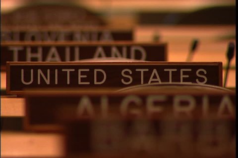 NEW YORK CITY - FEBRUARY 11, 1999: MCU row of wooden name signs for Algeria, United States and Thailand, camera zooms out to show MS of empty seats in  the United Nations General Assembly hall.