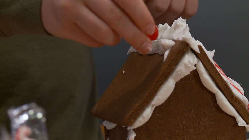 Detail of boy decorating a gingerbread house.