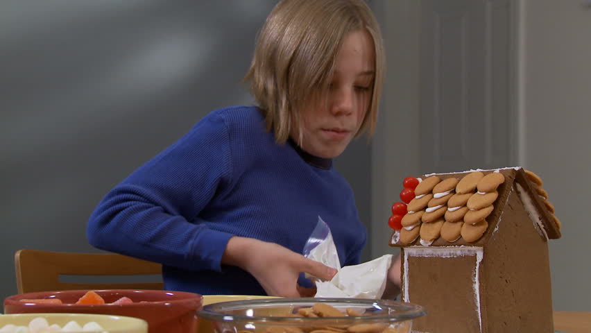 Boy decorating a gingerbread house.