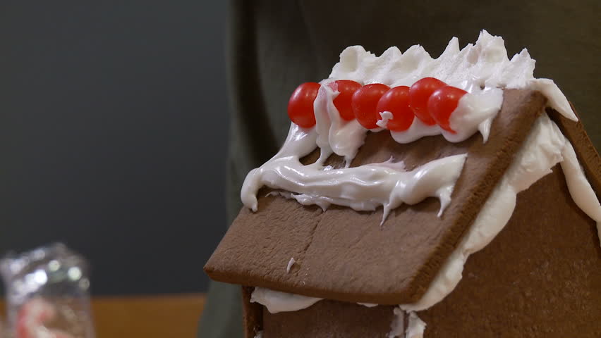 Detail of boy decorating a gingerbread house with red candies.