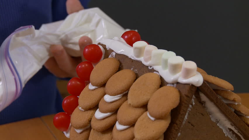 Boy's hand sticking small marshmallows on the roof of a gingerbread house.