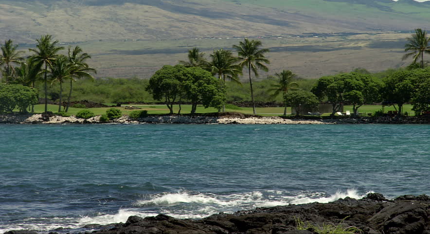 Clear blue water laps at rocky shore near a hotel in Hawaii