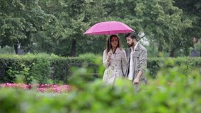 Young couple under umbrella walking among flowers in the park