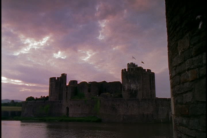 Caerphilly castle with moat in foreground under a pink cloudy sky in Caerphilly, South Wales.