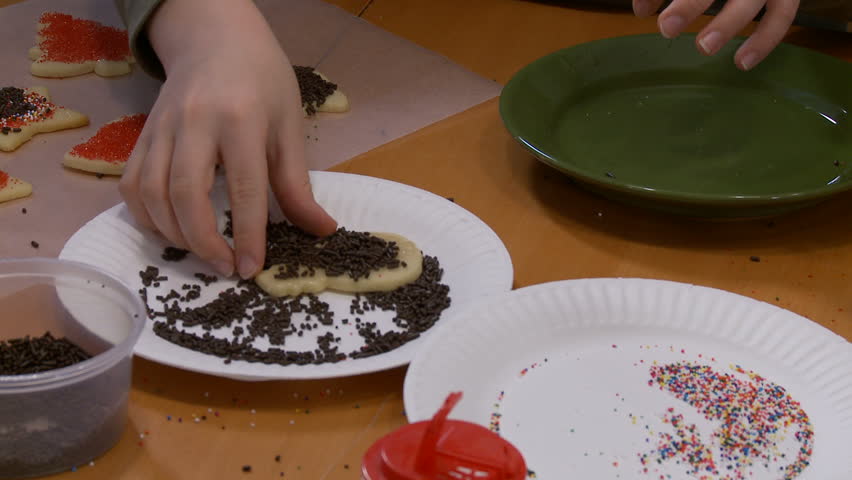 Boy decorating Christmas cookies then sucking the excess frosting off his
