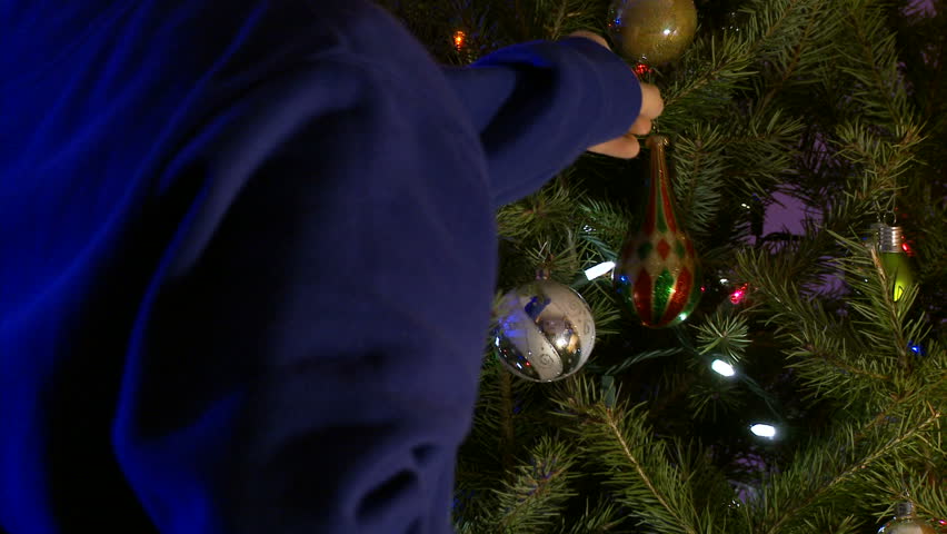 Child's hand hangs a multicolored ornament on a Christmas tree.