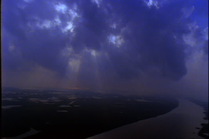 Bank of blue clouds with sun streaming through above the Mississippi River.