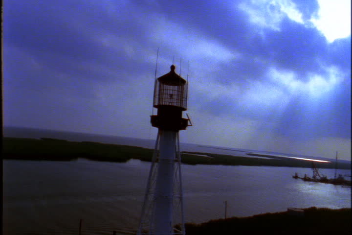 Lighthouse on bank of the Mississippi River under thick clouds with sun streaming through.