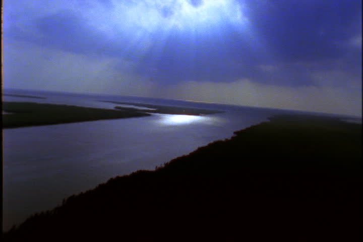 Aerial over the Mississippi River, camera tilts up to cluster of dark clouds with sun streaming through.