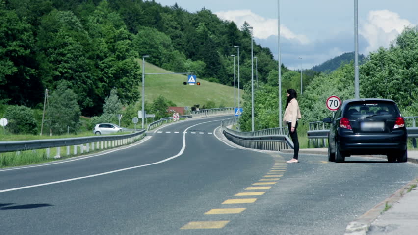 Woman standing by the road with broken car