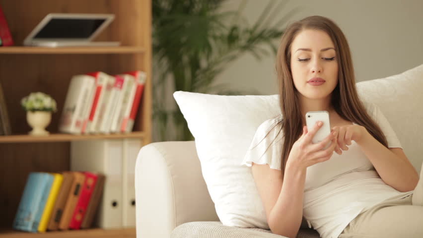 Attractive young woman on sofa using mobile phone and smiling