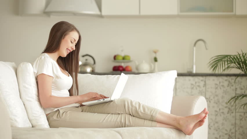 Attractive young woman chilling on sofa with laptop holding credit card and