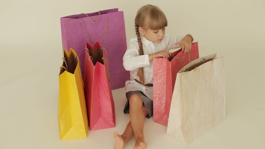 Beautiful little girl sitting on floor looking into shopping bags showing thumb