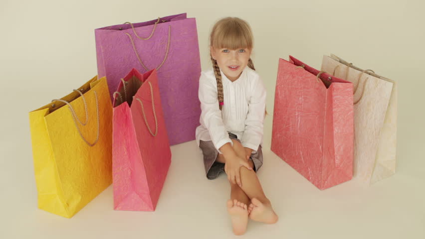 Cute little girl sitting on floor surrounded by shopping bags gesturing with