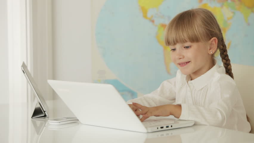 Beautiful little girl sitting at desk using laptop and touchpad and smiling at